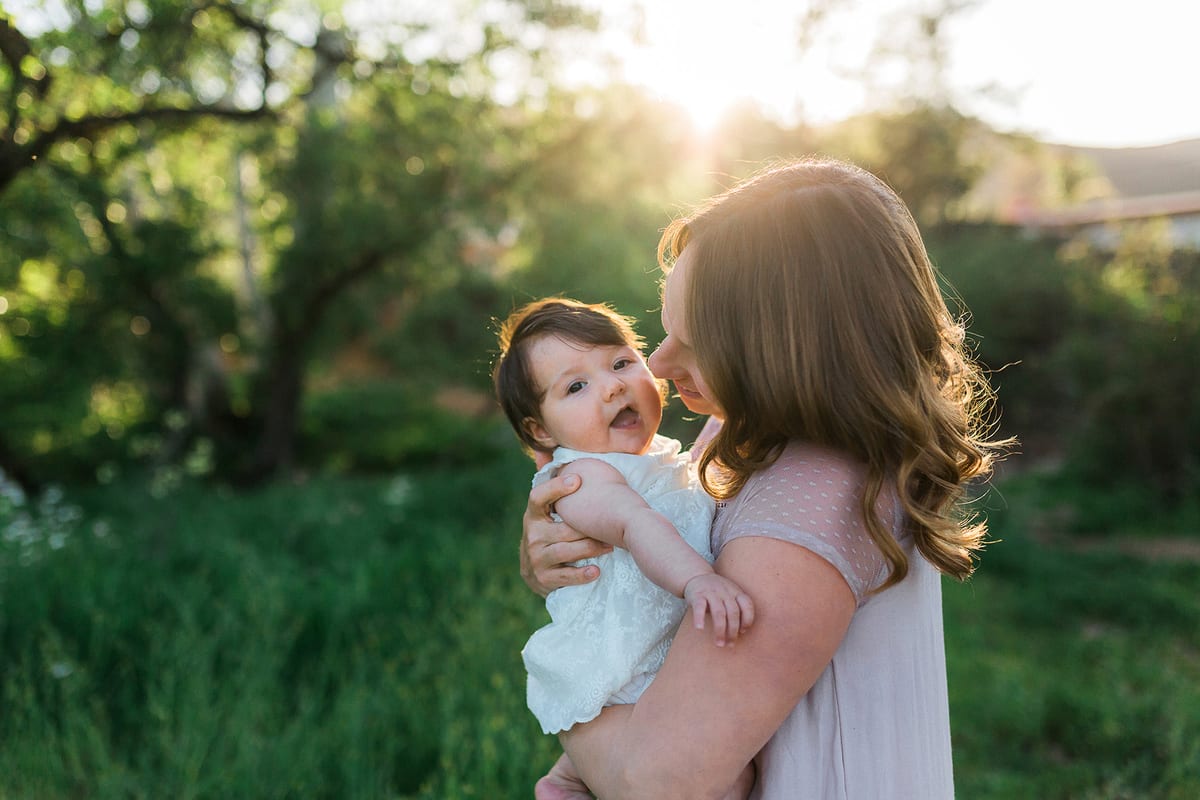 Mother holding her baby daughter up to her cheek in golden backlight