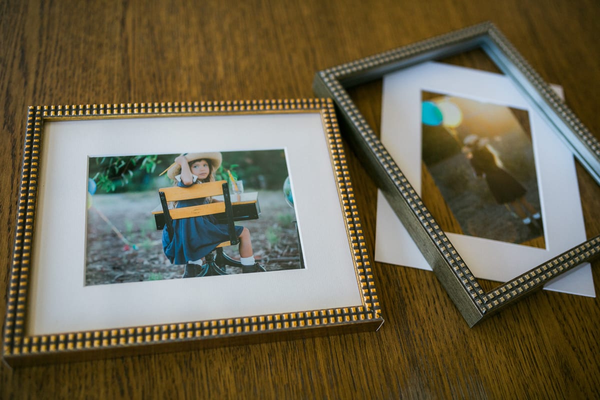 Two framed family prints in gold and silver frames on a wooden table
