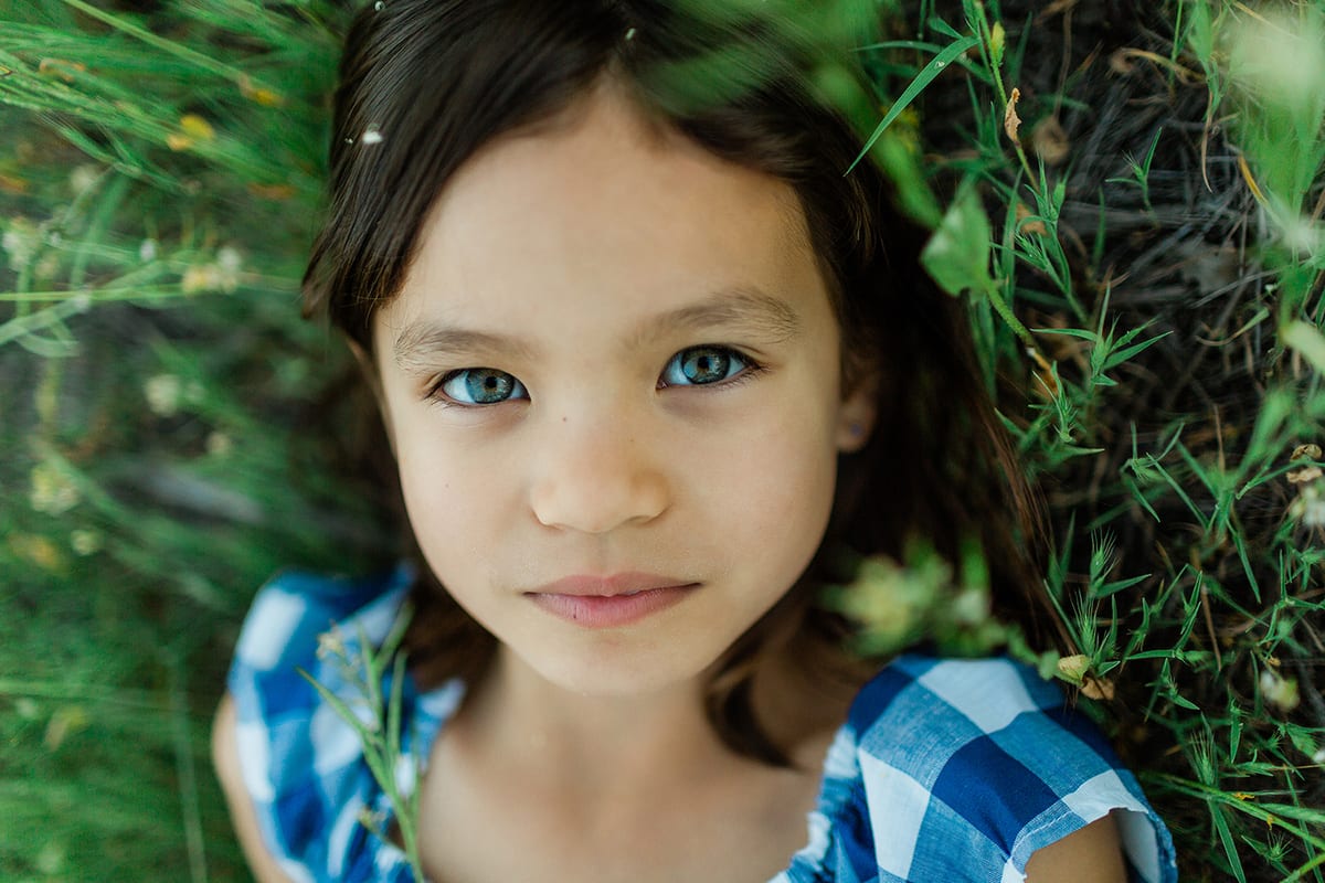 Close-up portrait of a girl with blue eyes lying in green grass