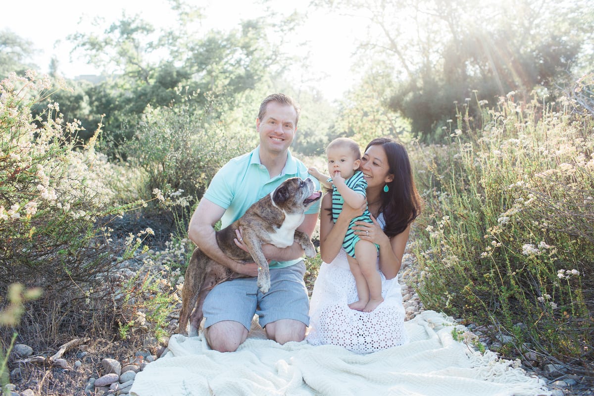 Family sitting on a blanket among wildflowers with their baby and bulldog