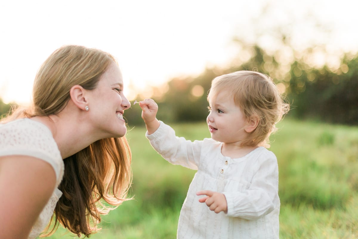 Toddler girl touching her mother's nose with a blade of grass