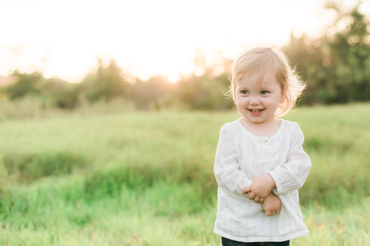 Smiling toddler girl in a white blouse standing in a green field