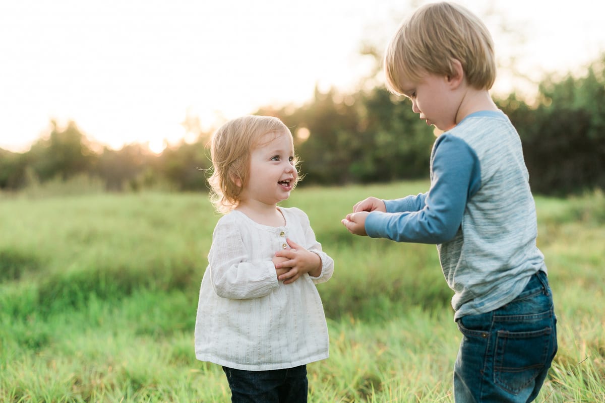 Toddler girl and her big brother playing in a green field