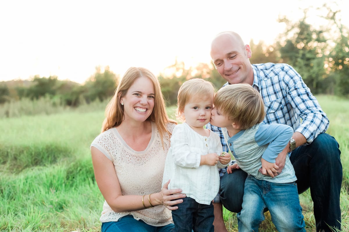 Parents with their two young sons sharing a kiss in the grass