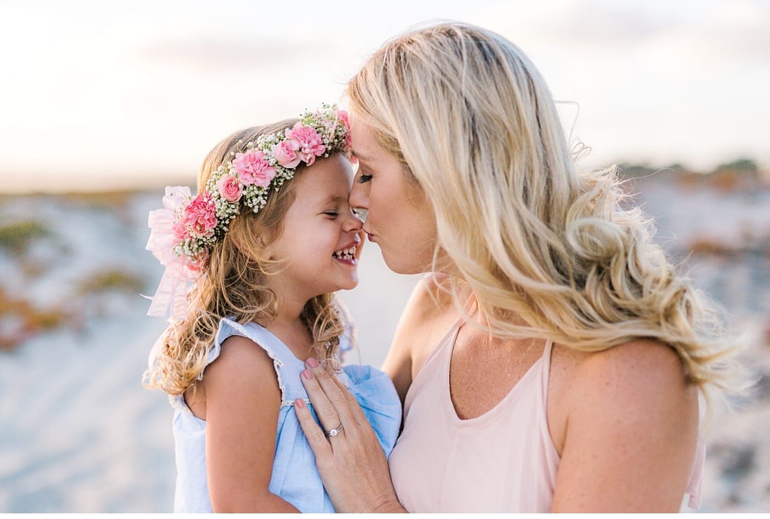 Mother and daughter in a pink flower crown touching noses in the sand dunes