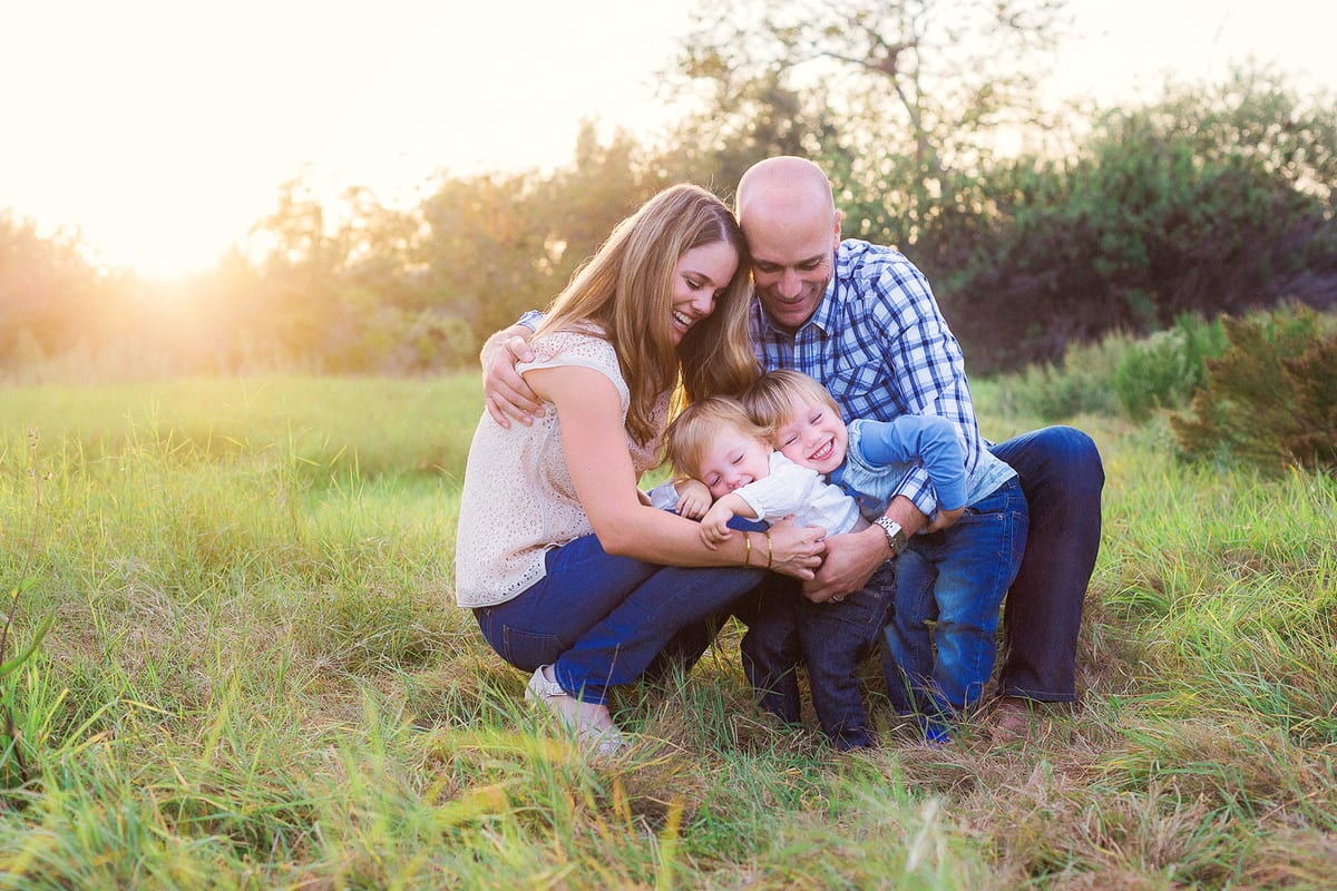 Parents cuddling their two little boys in a sunlit meadow
