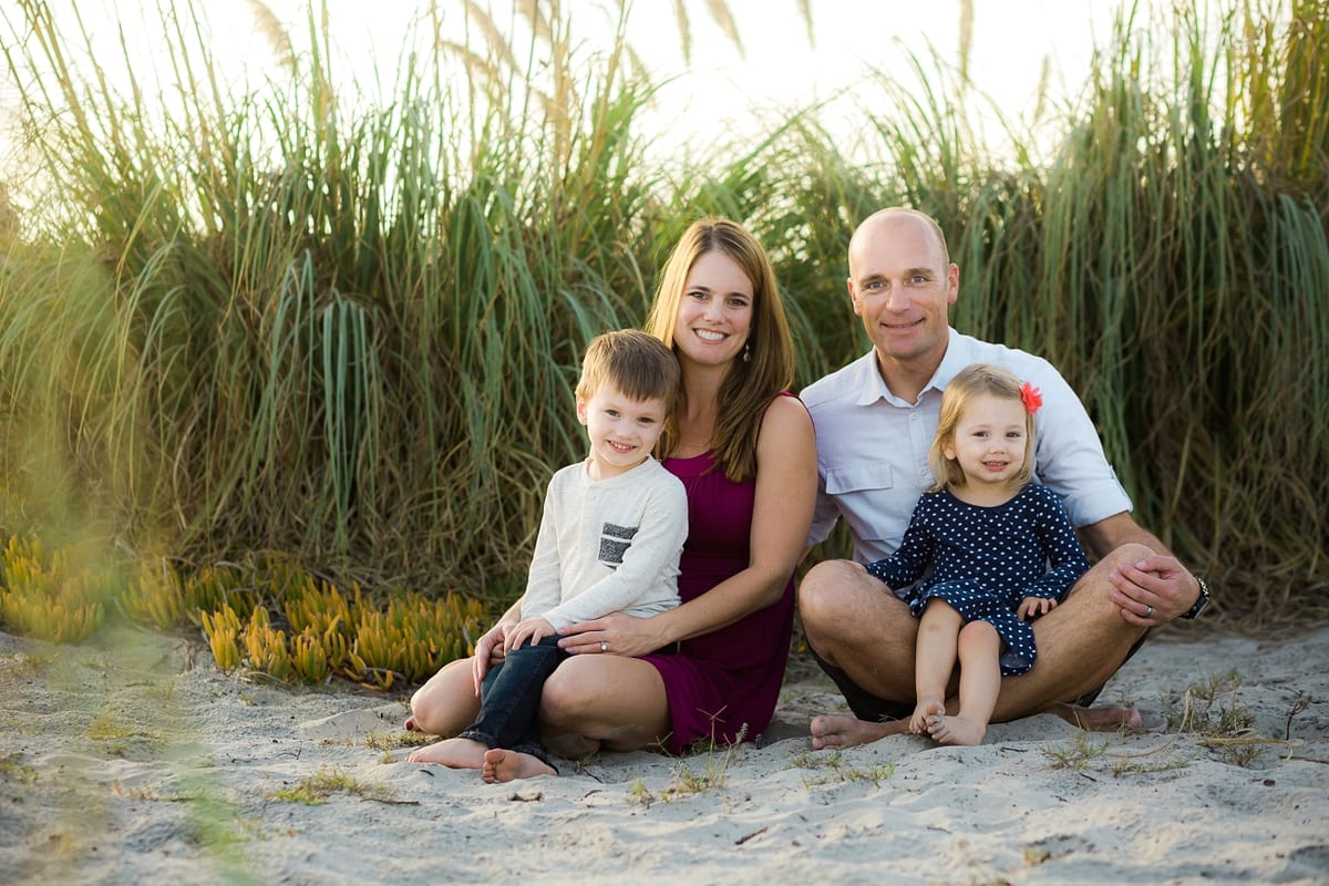 Parents sitting in the sand with their son and daughter in front of tall beach grass