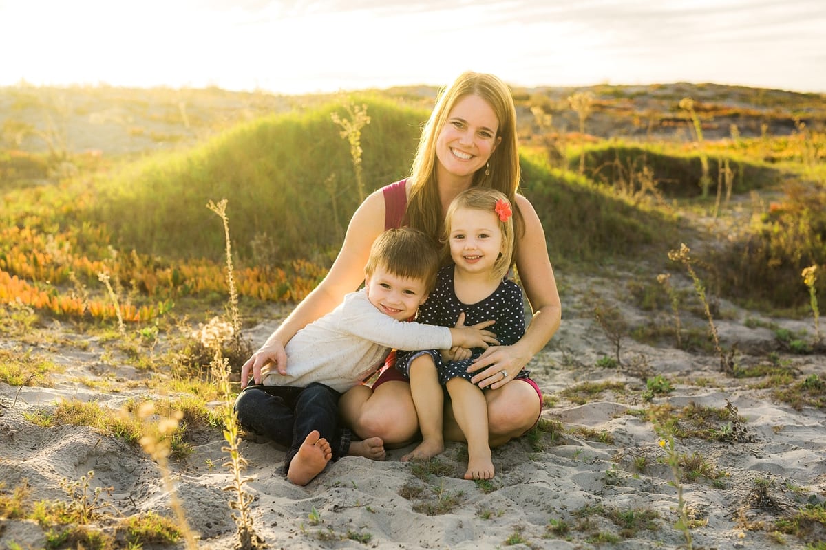 Mother sitting in the sand dunes hugging her son and daughter