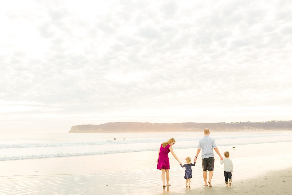 Family walking hand in hand along the shore toward Point Loma