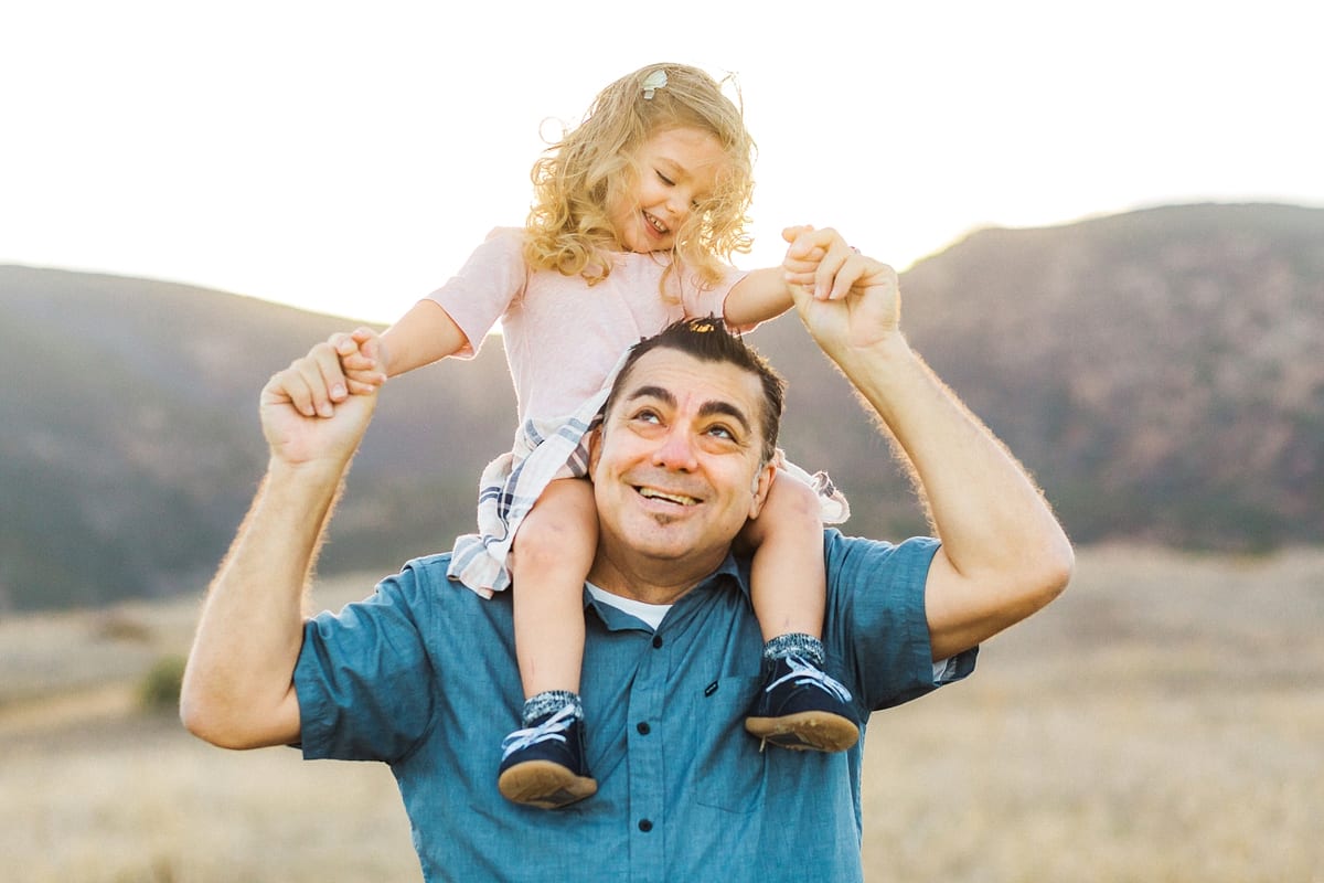 Father carrying his laughing daughter on his shoulders in the hills