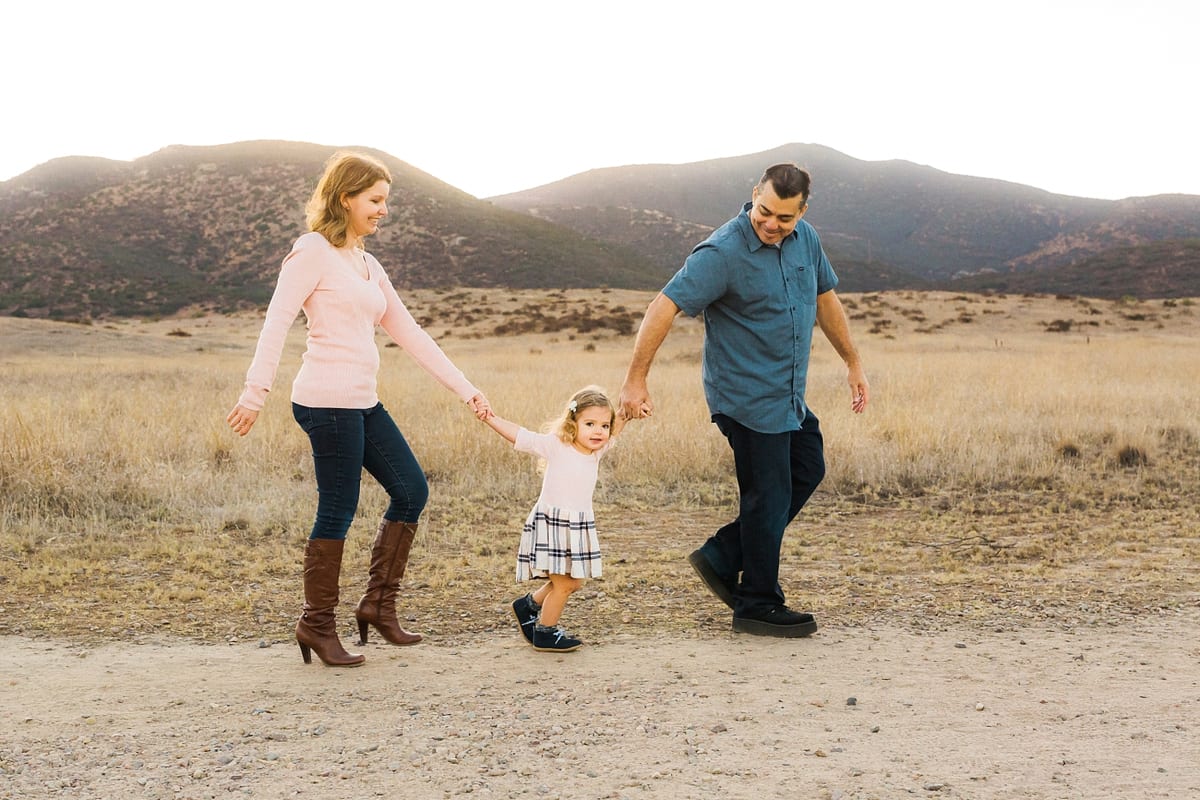 Parents swinging their little girl between them on a dirt path