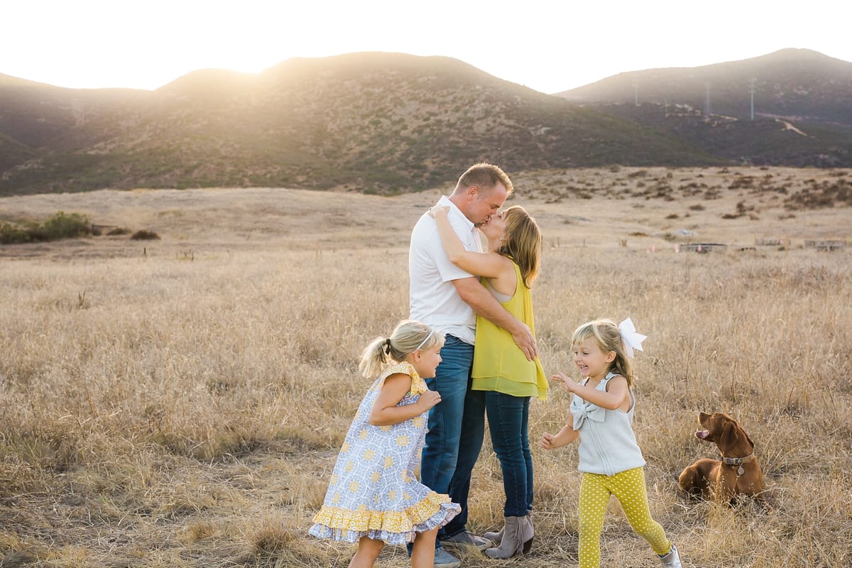 Father hugging his daughter as her younger sisters play with the dog in a golden field