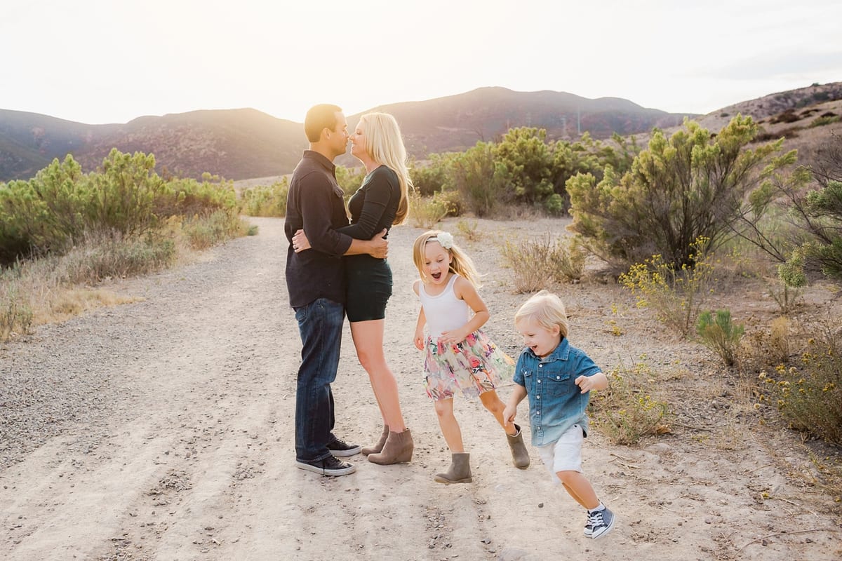Parents kissing on a dirt trail as their children dance beside them