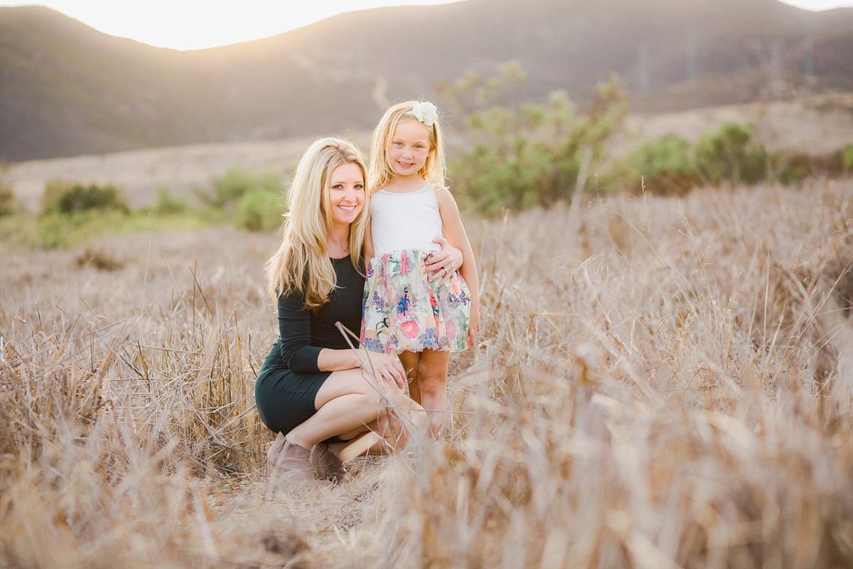 Mother kneeling beside her daughter in a field of golden grass