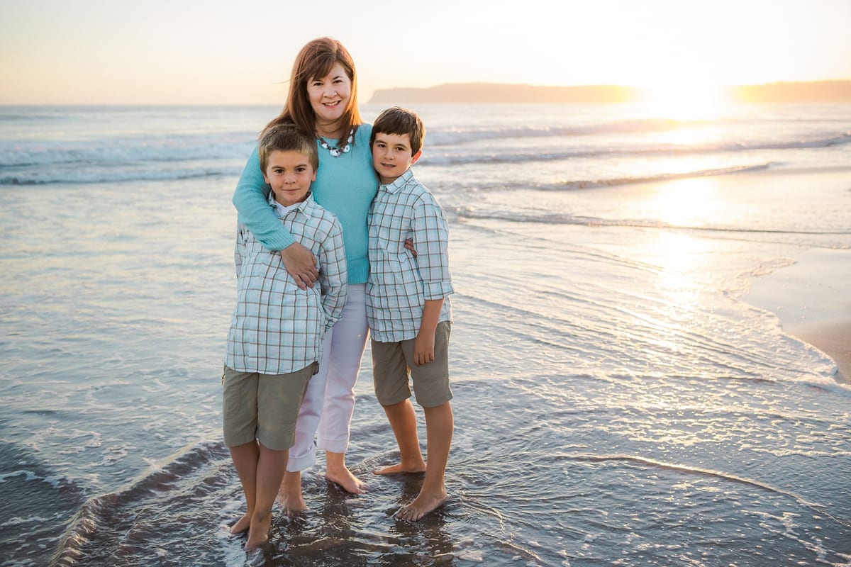 Mother with her two sons standing in the surf at sunset
