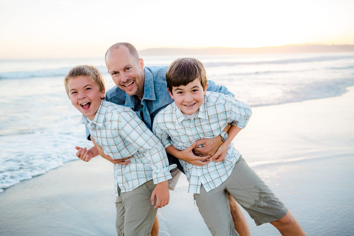 Father hugging his two laughing sons on the beach