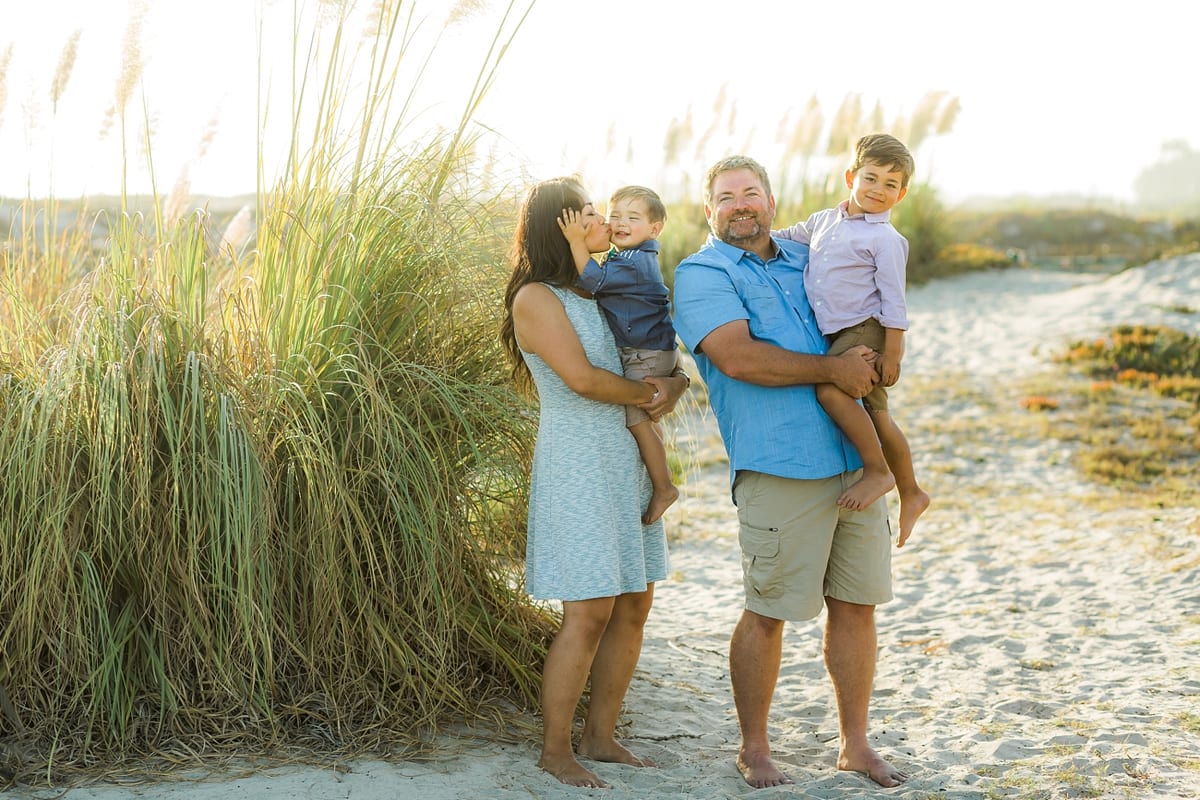 Parents holding their two sons beside tall beach grass