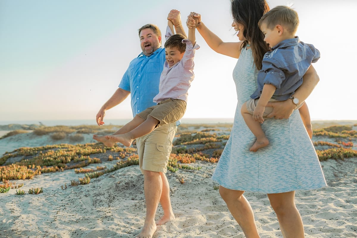 Father and mother swinging their boys playfully in the sand dunes