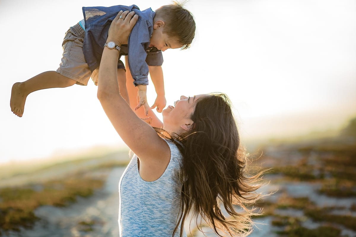 Mother lifting her son high into the air at the beach