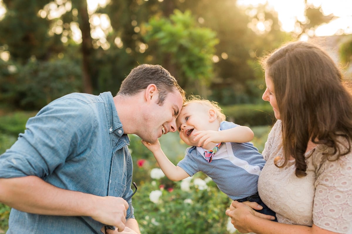 Father nuzzling his toddler son while mother smiles in a rose garden