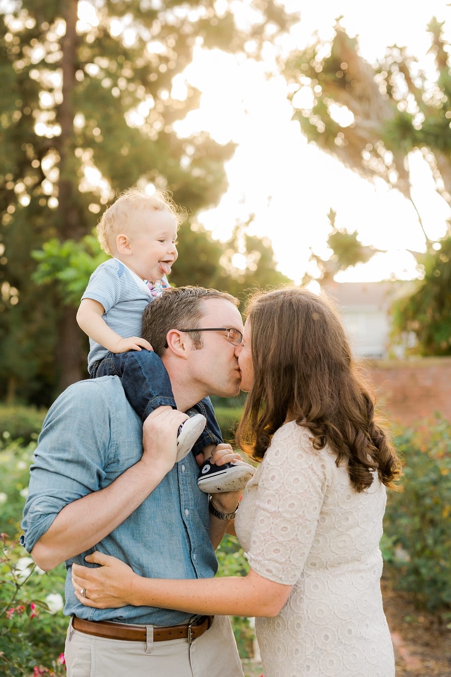 Father carrying his toddler on his shoulders while kissing his wife