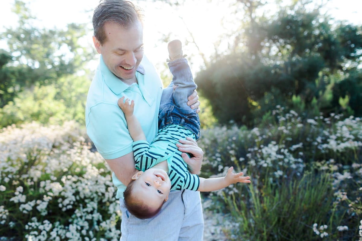 Father holding his baby son upside down among white flowers