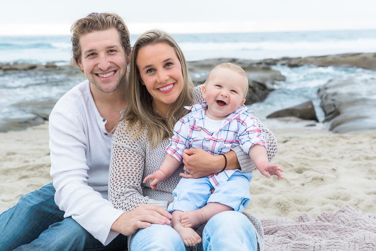 Parents with their laughing baby sitting on a blanket at the beach