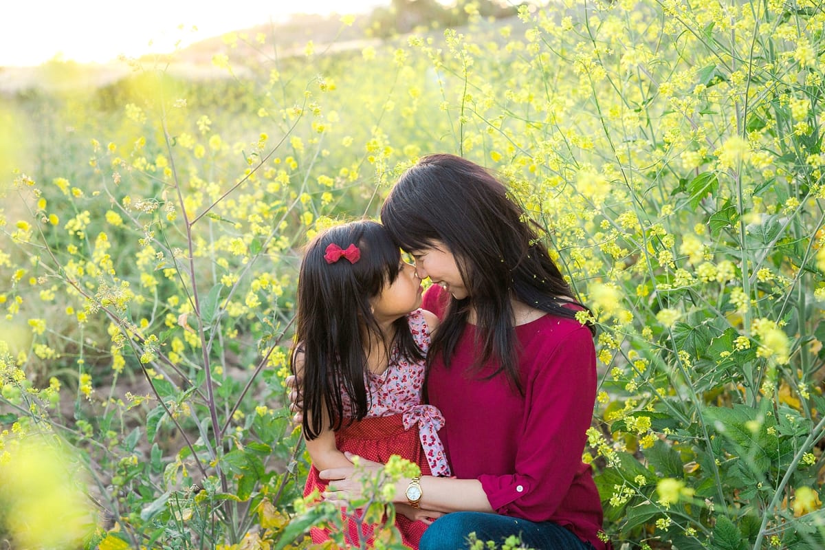 Mother and daughter touching noses among yellow wildflowers