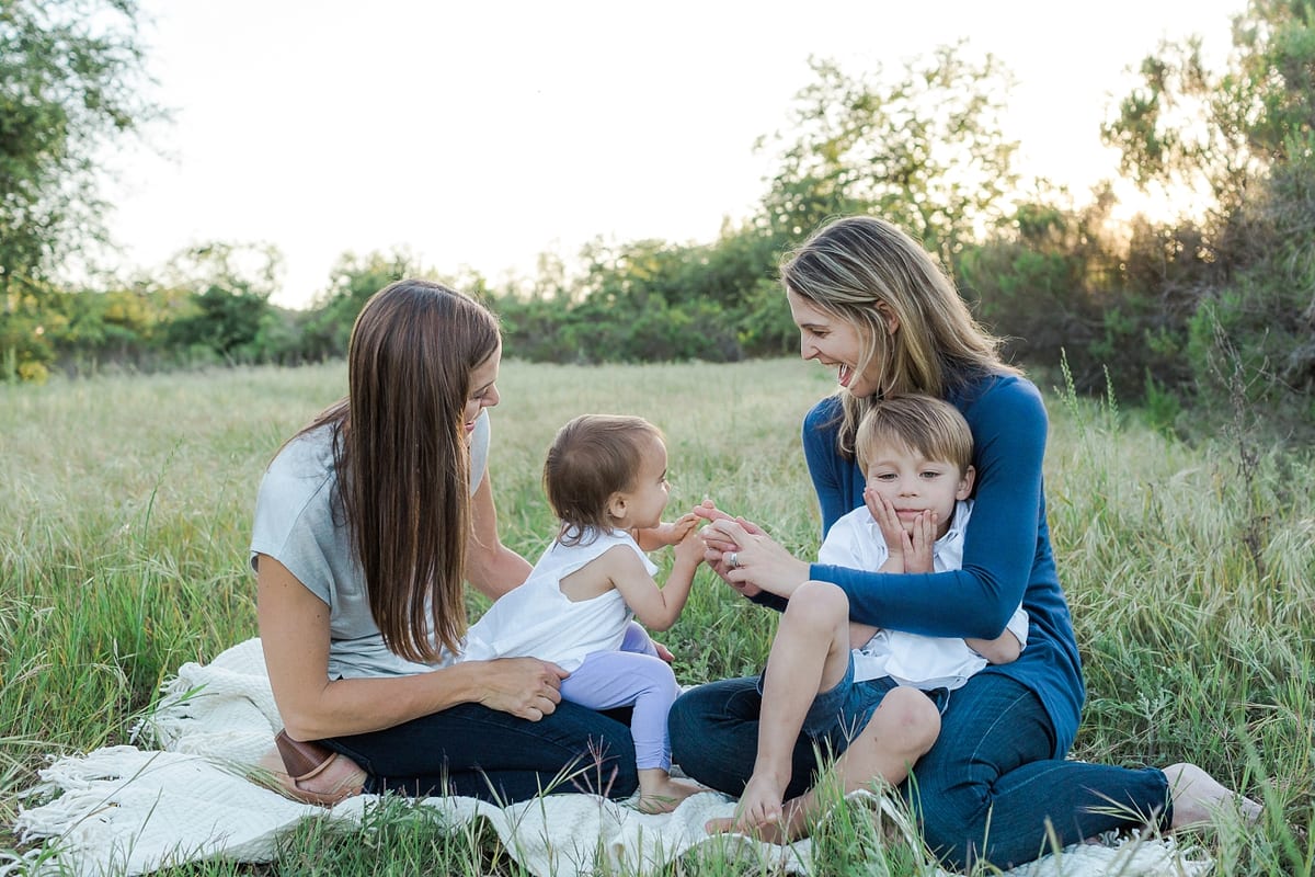 Two mothers sitting on a blanket in the grass with their toddlers