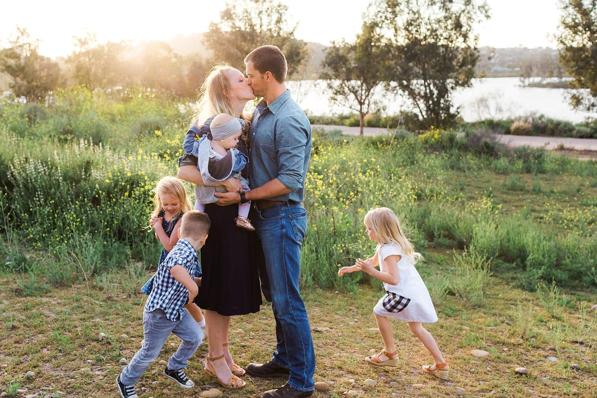 Parents kissing while their children play around them in a sunny field