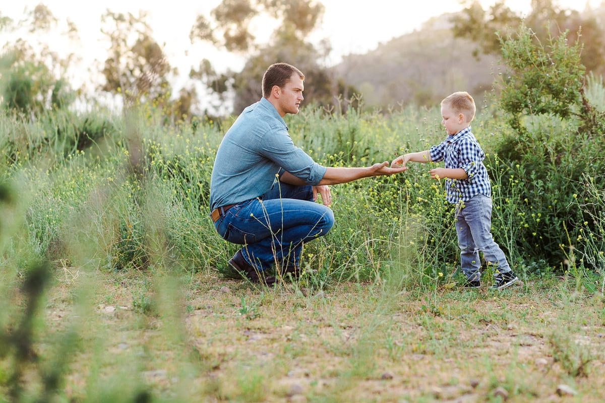 Father kneeling in a meadow holding his young son's hand