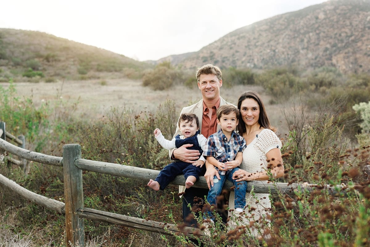 Parents with their two young sons sitting on a wooden fence in the hills