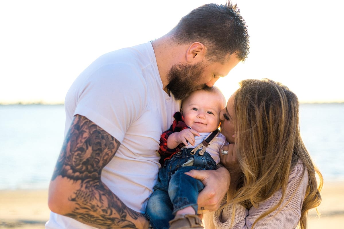Father kissing his baby son's head as mother kisses his cheek by the bay