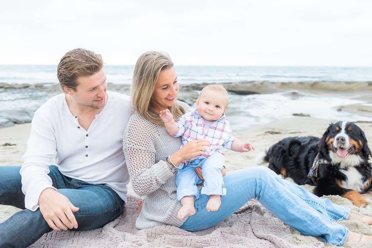 Parents sitting on the beach with their baby and their Bernese Mountain Dog
