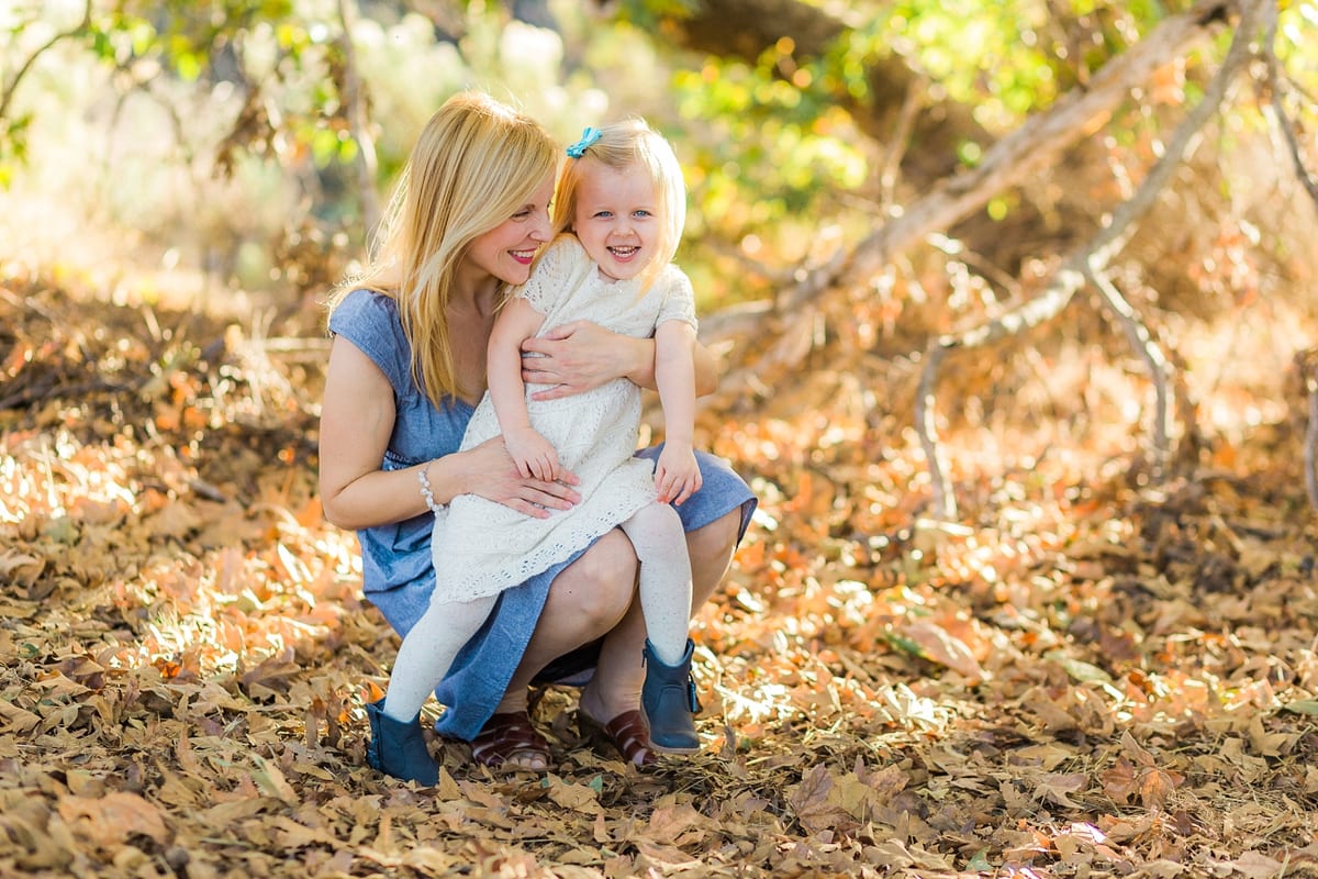 Mother crouching in autumn leaves hugging her toddler daughter