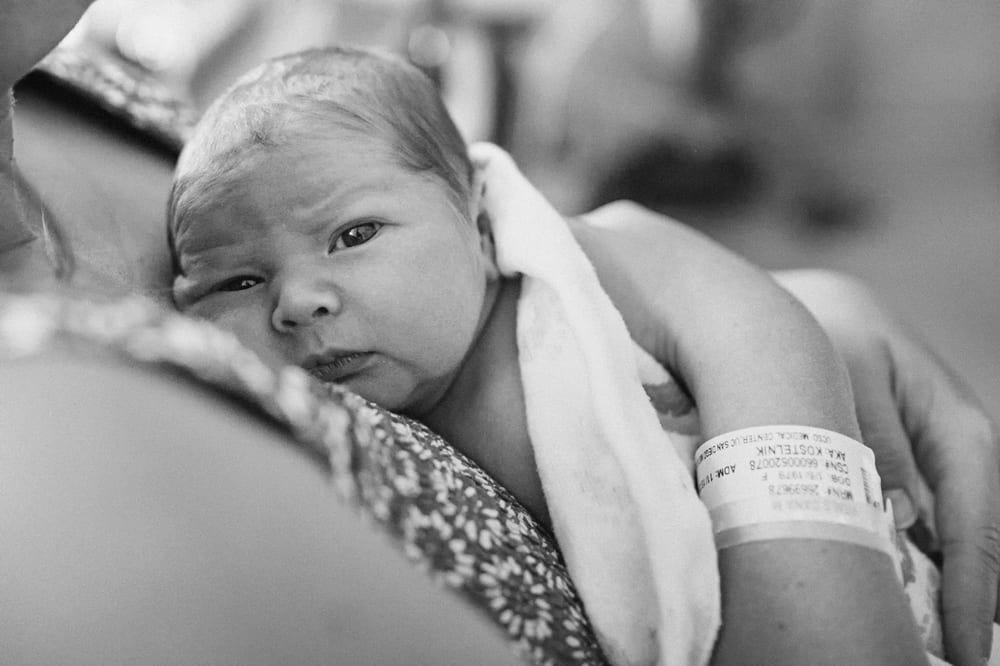 Black and white photo of a newborn resting on her mother's chest in the hospital