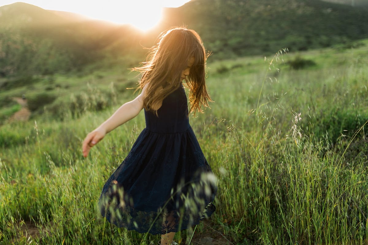 Girl in a navy dress twirling in a green hillside meadow at sunset