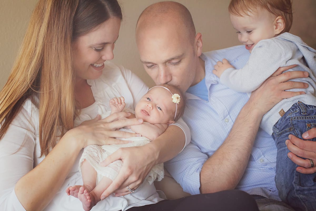 Father kissing his newborn daughter as mother and big sister look on