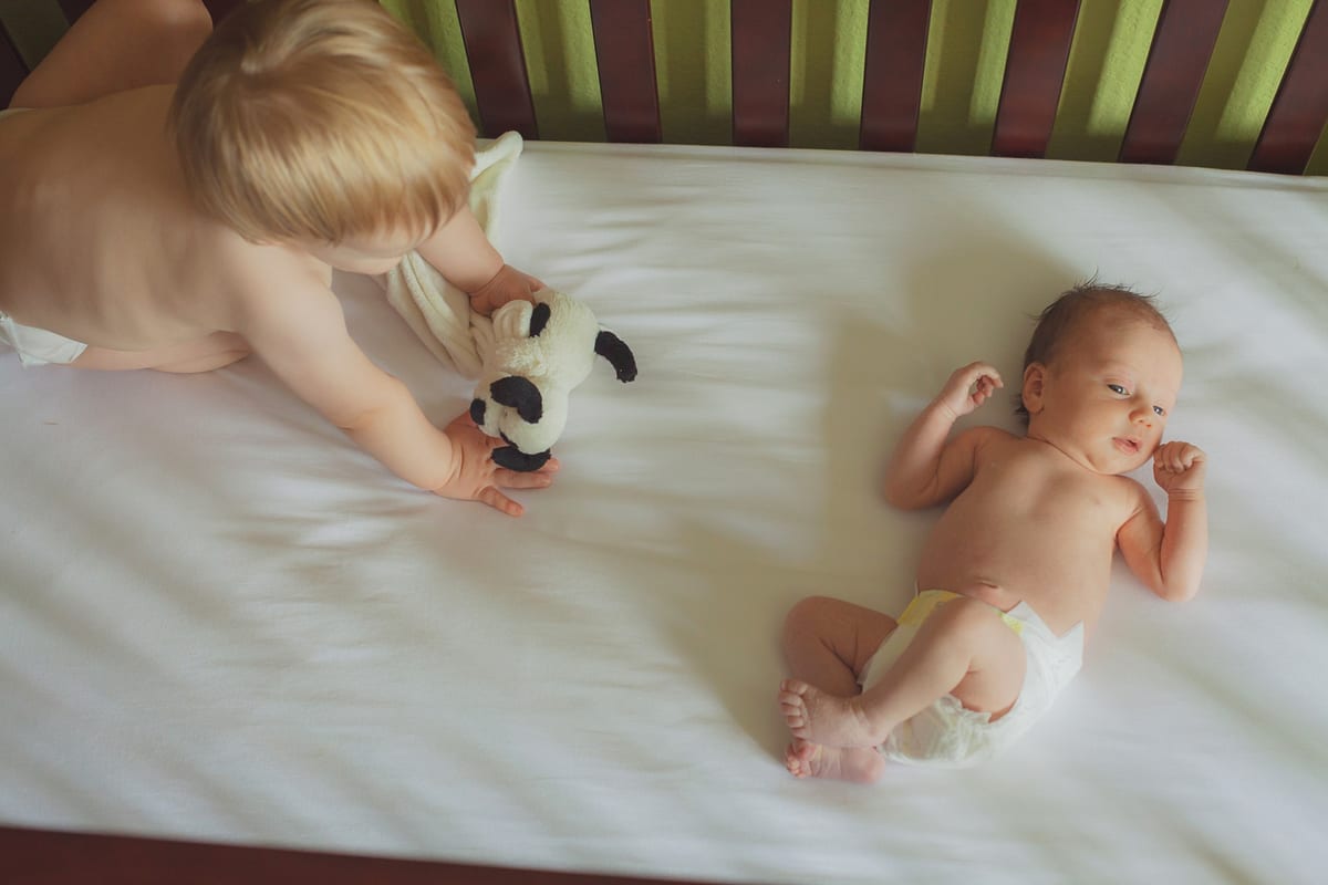 Big brother reaching toward his newborn sibling in the crib