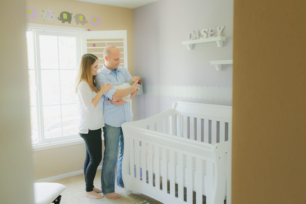 Parents holding their newborn in the nursery beside a white crib