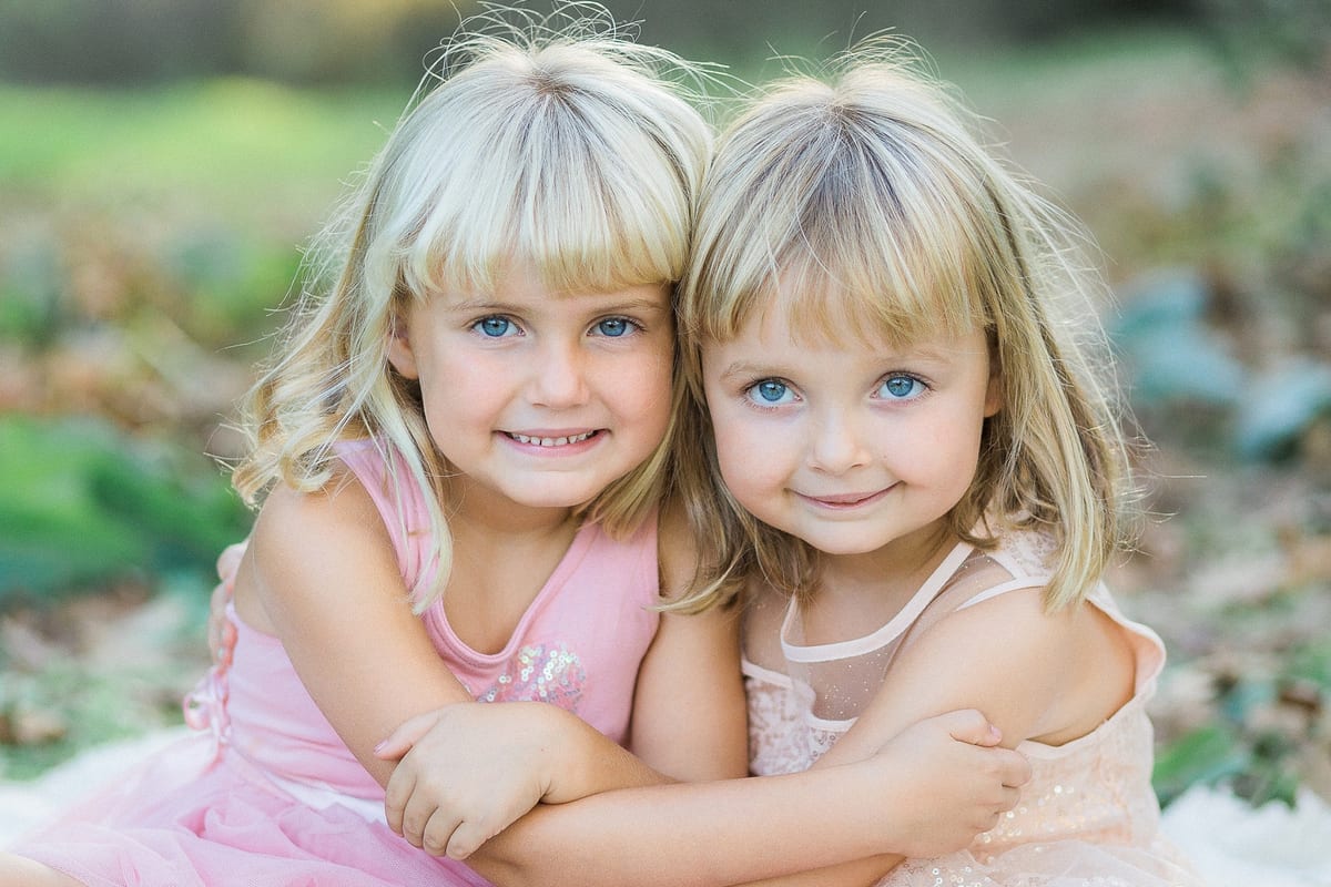 Two blonde sisters in pink hugging and smiling