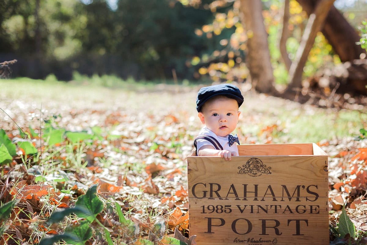 Baby boy in a newsboy cap sitting in a wooden crate among fall leaves