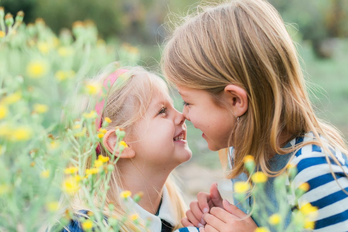 Two sisters touching noses among yellow wildflowers