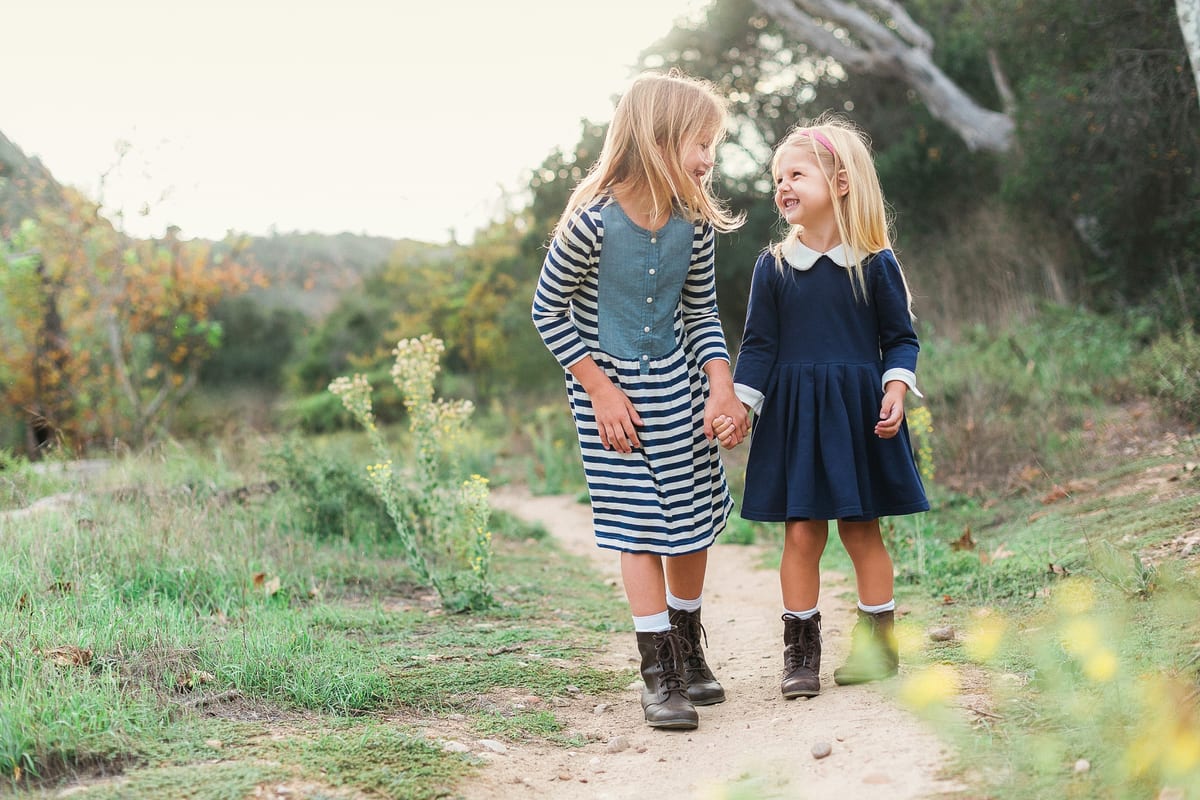 Two sisters holding hands and laughing on a dirt path
