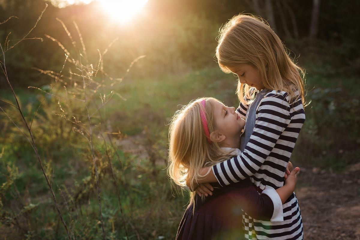 Big sister hugging her little sister in golden backlight