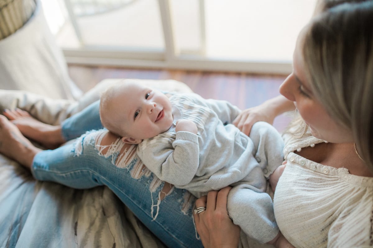 Baby grinning up at his mother as he lies across her legs
