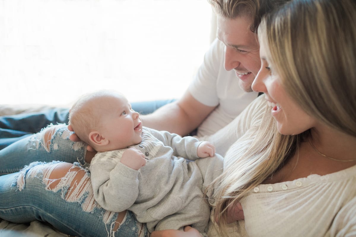 Parents leaning in to smile at their baby on the bed