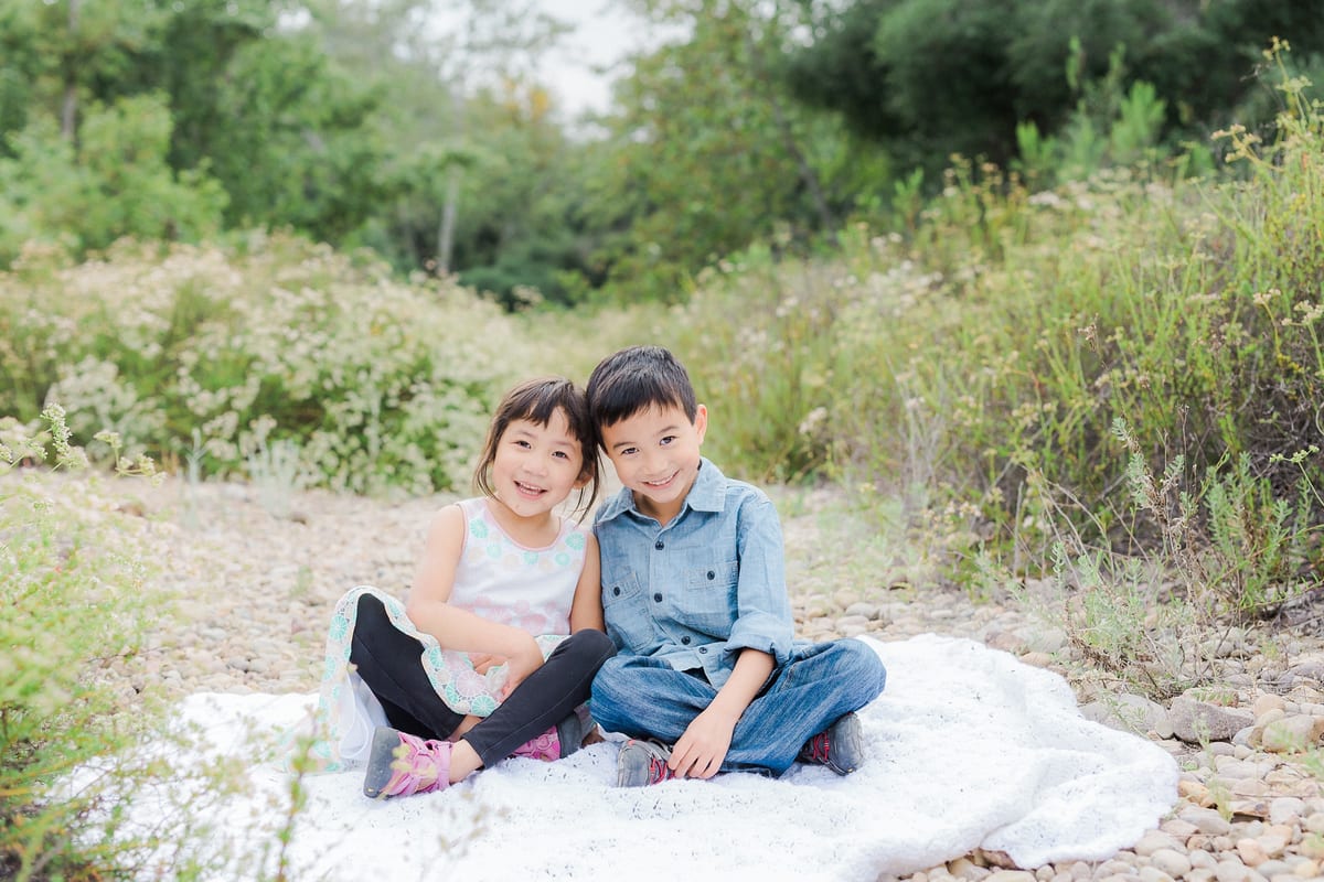 Brother and sister sitting together on a blanket by a creek