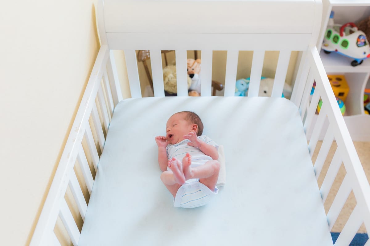 Newborn lying in a white crib seen from above