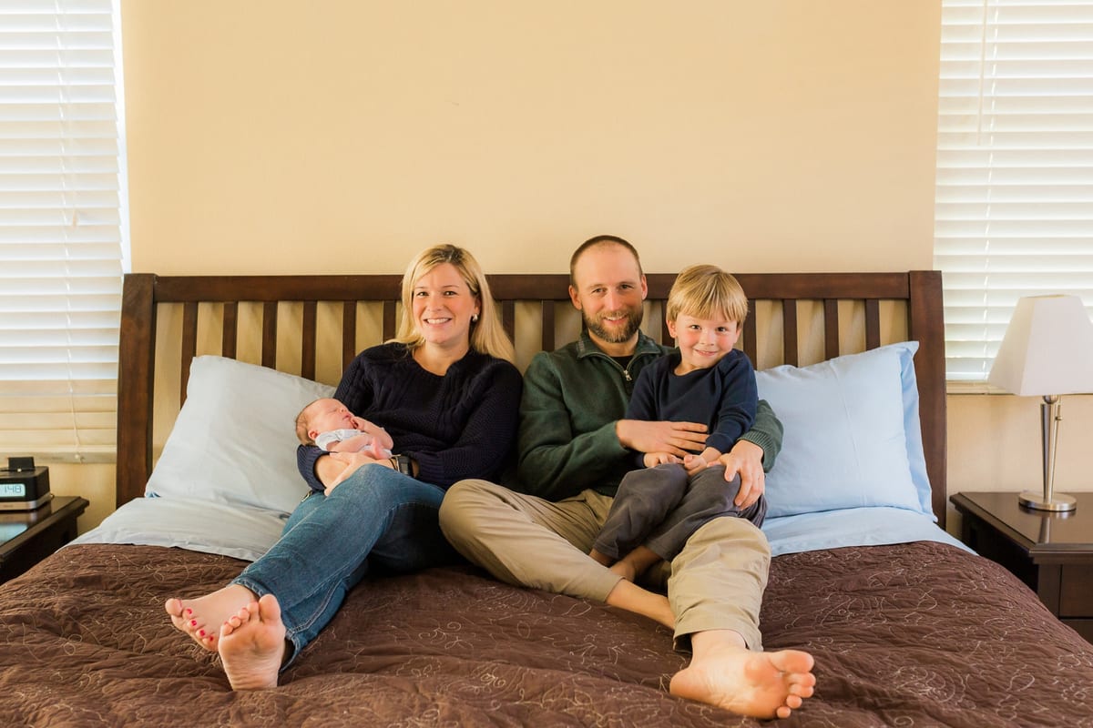 Parents and big brother sitting on their bed with the newborn